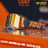 100% Armega MX 400goggles in orange and black with a reflective gold mirror lens, displayed on an orange reflective surface with promotional text overlays.